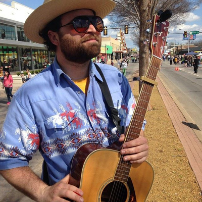 Handsome Casey Friedman, Oklahoma musician, stands with acoustic guitar while busking at Open Streets in the Uptown 23 district.